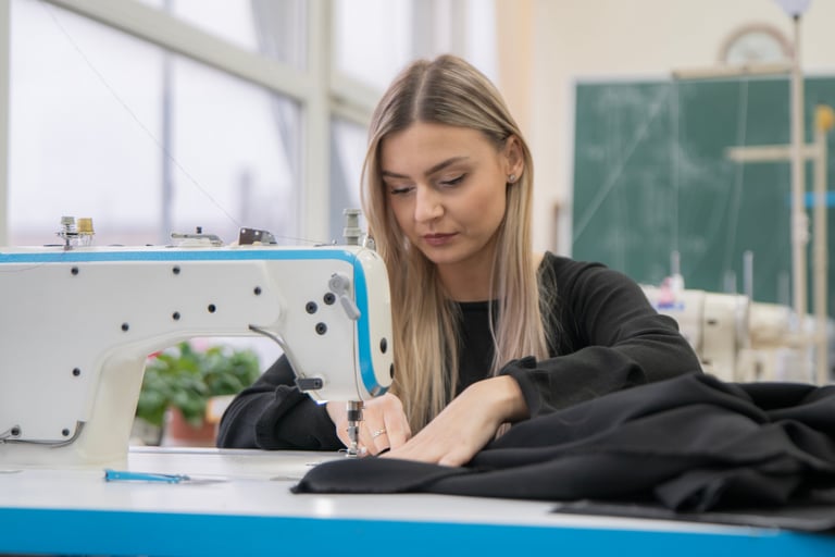 A skilled seamstress carefully stitches fabric on a sewing machine, surrounded by sunlight in a vibrant workshop