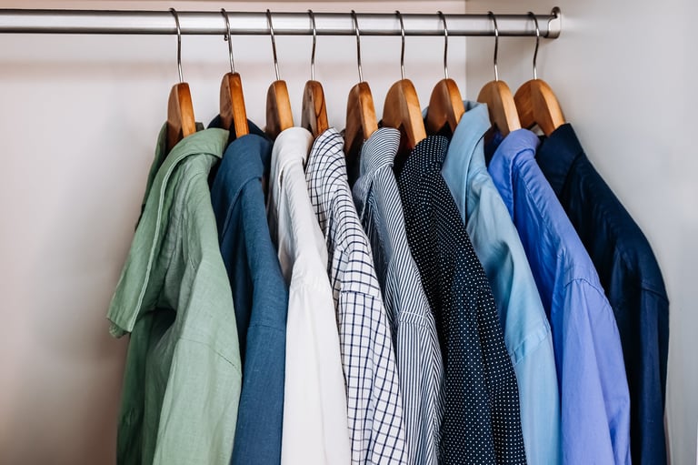 Color-sorted shirts hanging on wooden hangers inside a clean, modern wardrobe